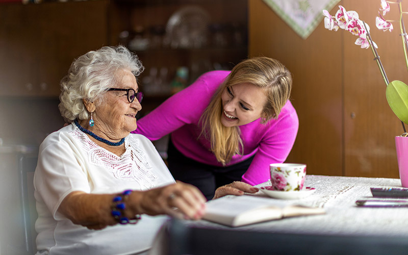 A woman helping an older woman with a cup of tea.