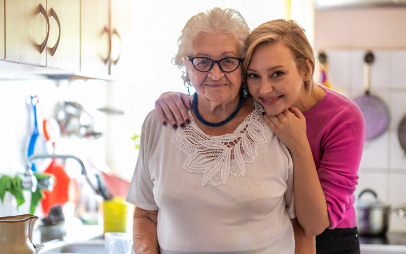 A woman hugging an older woman in a kitchen.